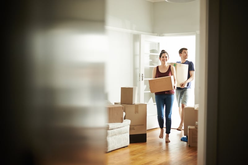 A man and a woman carry boxes into a new house.