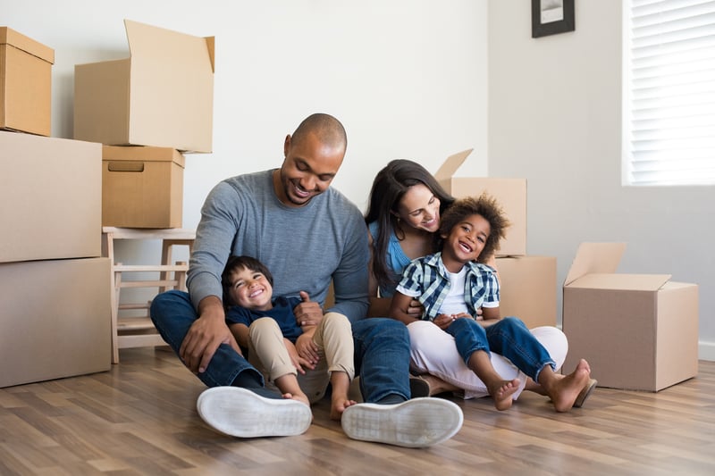 A family sits on the floor surrounded by moving boxes.