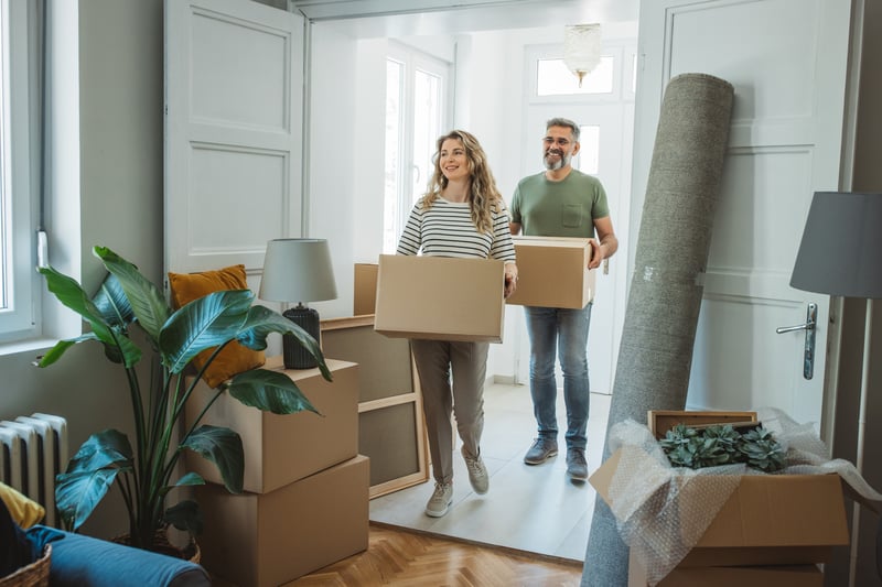 A man and woman carry boxes into a new house.