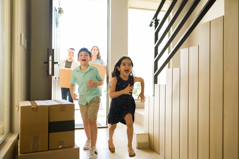 Kids run into a new house while their parents carry boxes in behind of them.