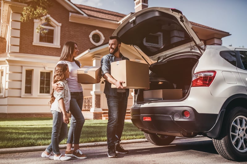 A family unloads boxes from a car while moving into a new house.