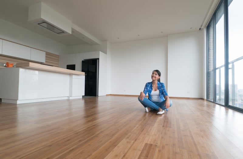 A woman sits on an empty living room floor while moving into a new house.