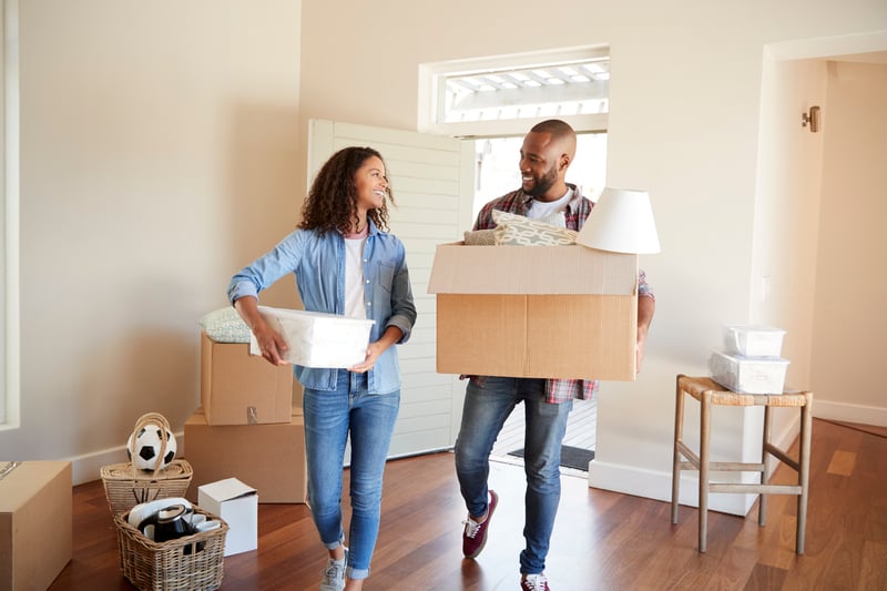 A man and a woman carry boxes into their new house.
