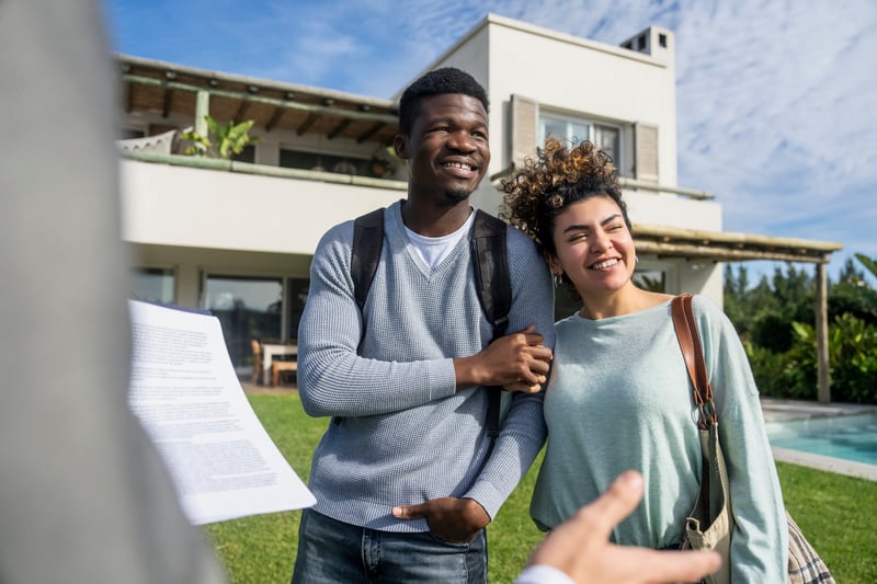 A man and woman smile outside of a home purchased with a jumbo loan.