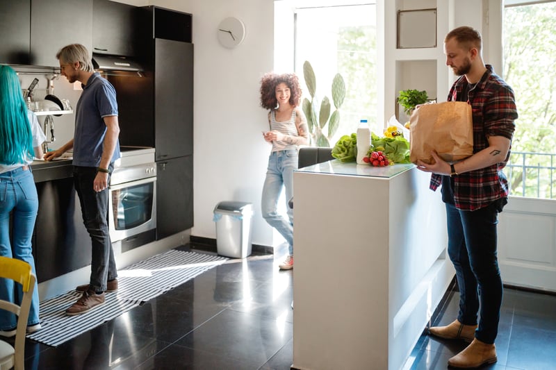 A man and a woman carry boxes into the kitchen of their new home.