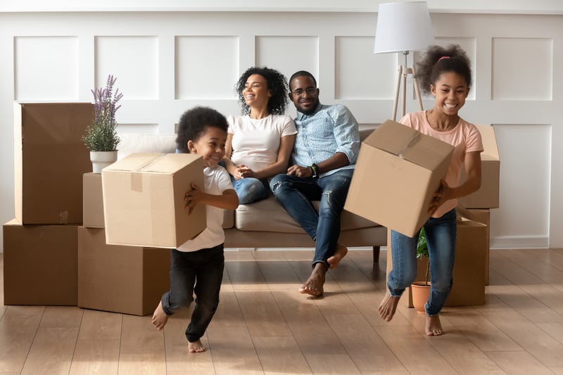 A family of four carries boxes into a new house.