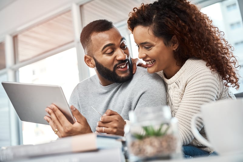 A man and a woman smiling while looking at a tablet.