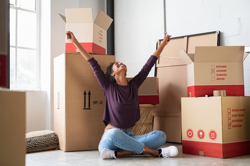 A woman celebrates after carrying boxes into a new house.