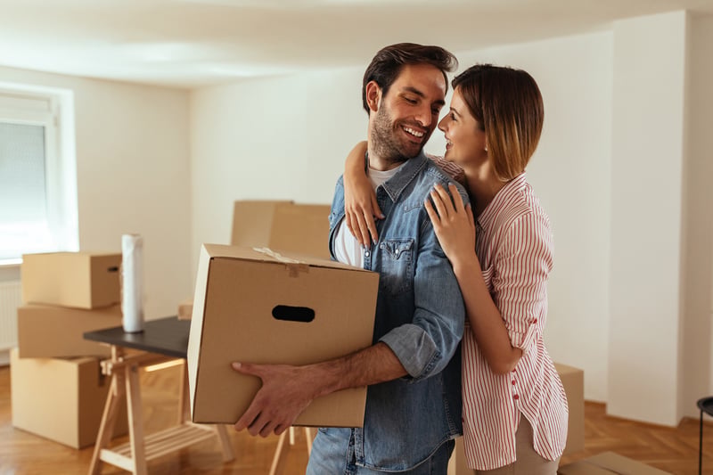 A man and a woman carry boxes into a new home.