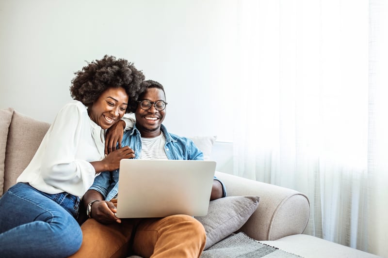 A man and a woman smile while looking at a laptop.