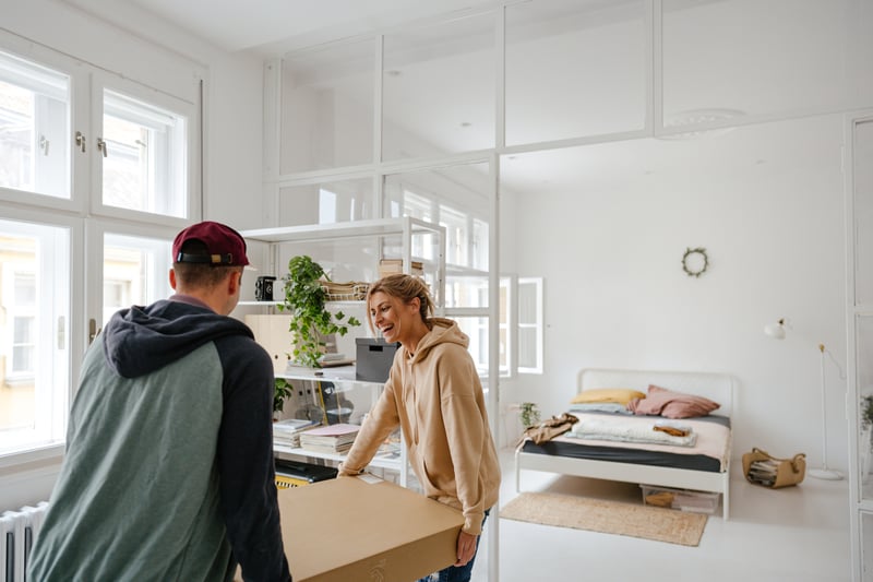 A man and a woman smile while carrying a box into a house.