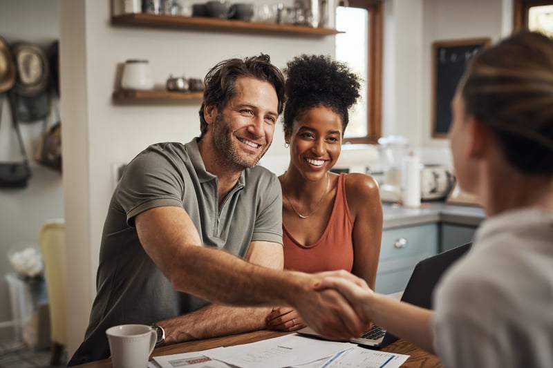 A couple shakes hands with a real estate agent.