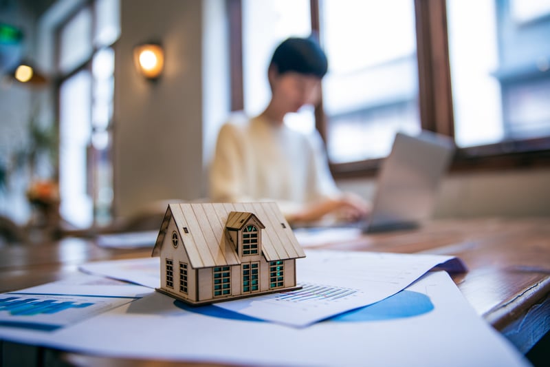 A mortgage rate illustration with a small wooden house on a stack of papers.