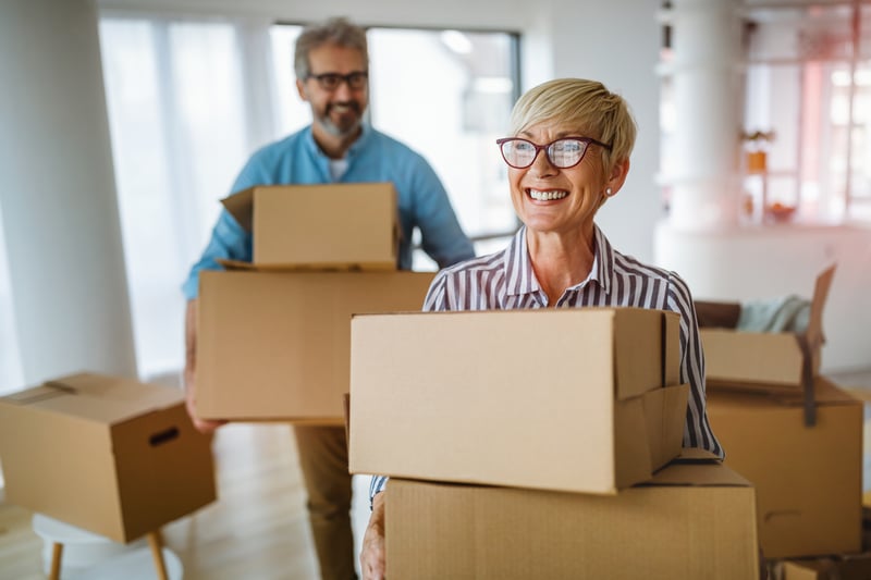 A man and a woman carry boxes into a new house.