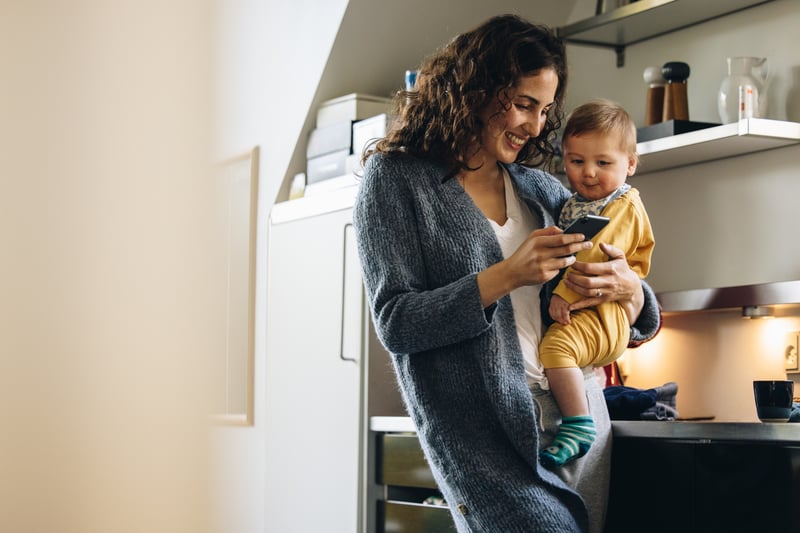 A woman smiles at a phone while holding a young child.