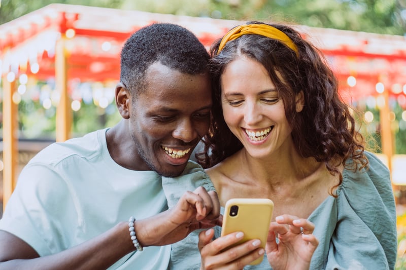 A man and a woman smile while looking at a phone.