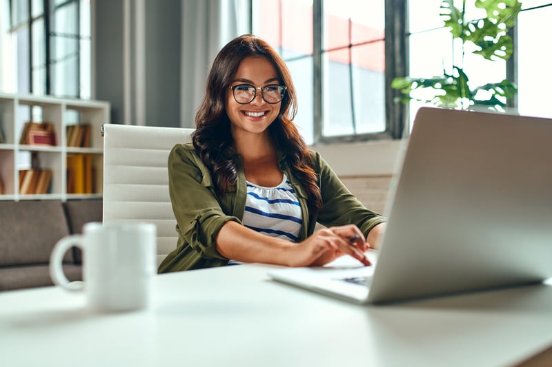 A woman smiling while working at a laptop. 