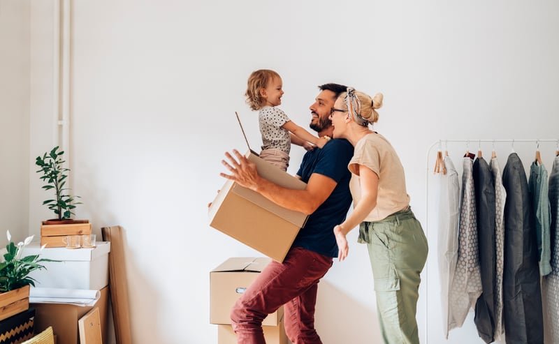 A family of three carries boxes into a new home.