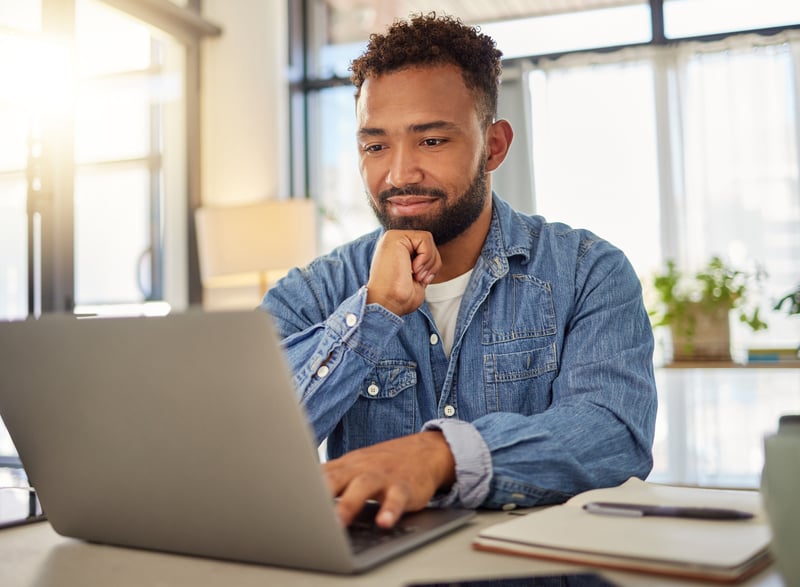 A man smiles at a laptop while comparing DSCR and conventional loans.