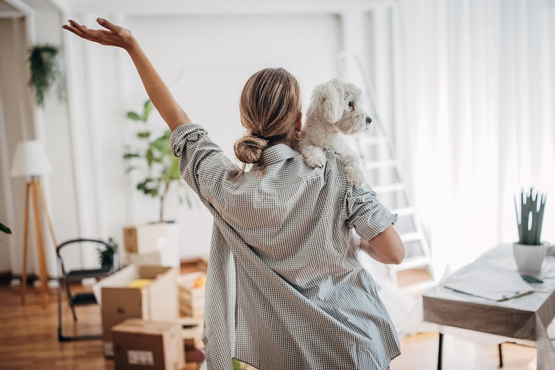 A woman carries a bichon frise into a new house.