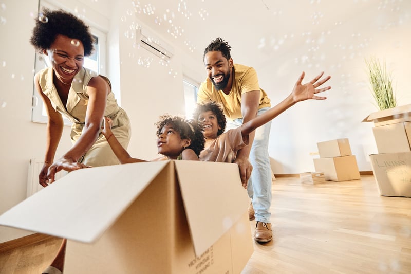 A family pushes their kids around in a box while moving into a new house.