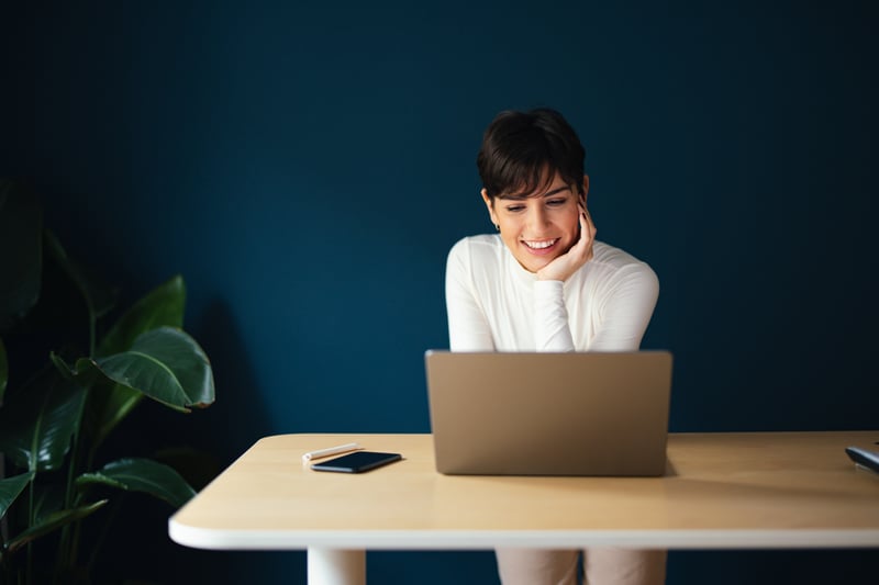 A woman smiles at a laptop while comparing loan estimates.