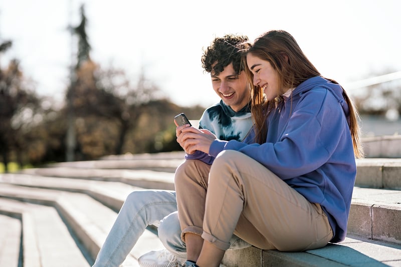A man and a woman smile at a phone while exploring Maryland refinance rates.