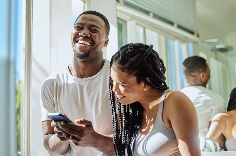 A man and a woman laugh while looking at a cell phone.