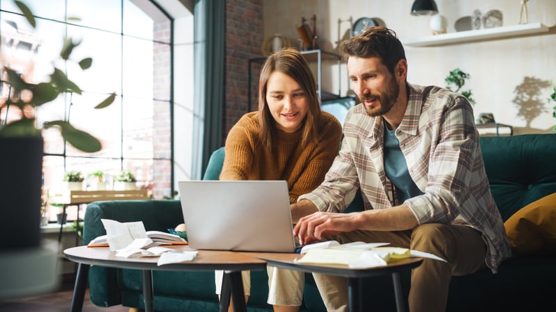 A woman and a man smiling while looking at a laptop.