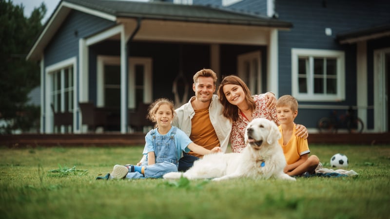 A family sits in the yard of their second home with their dog.