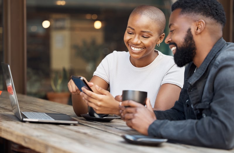 A man and woman drink coffee and smile at a cell phone.