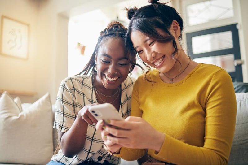Two women smile at a phone.