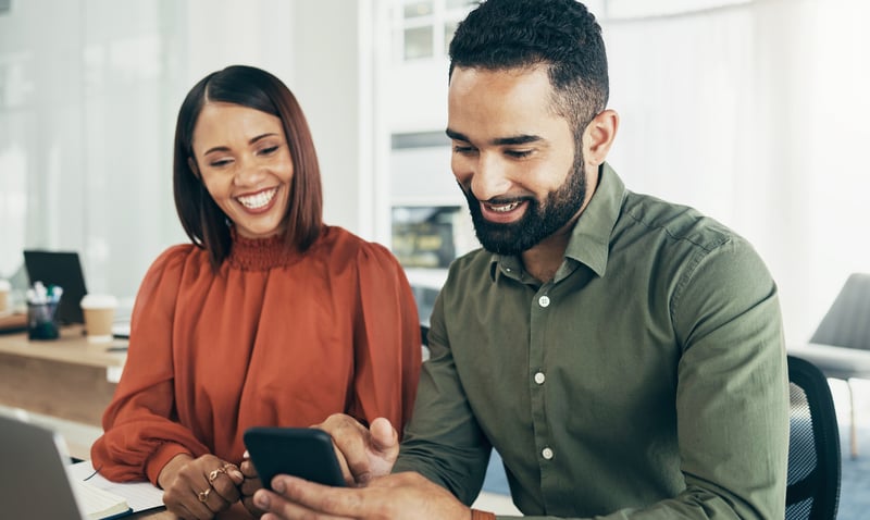 A man and a woman smile while reviewing Montana refinance rates on cell phone.