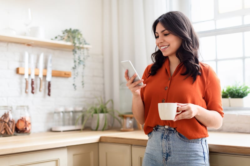 A woman drinks coffee and reviews refinance options on her phone.