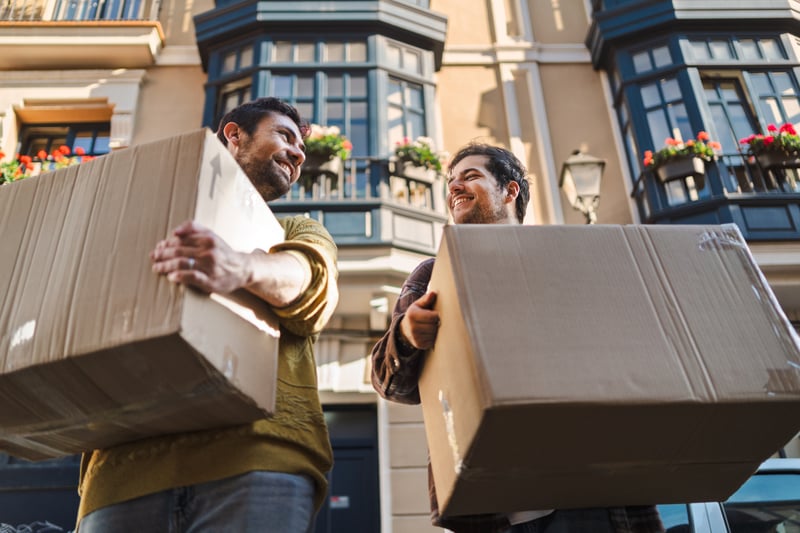 A couple smiles while carrying boxes into a new house.