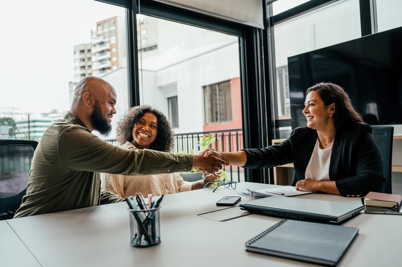 A man and woman shake hands with an agent while closing on a house.