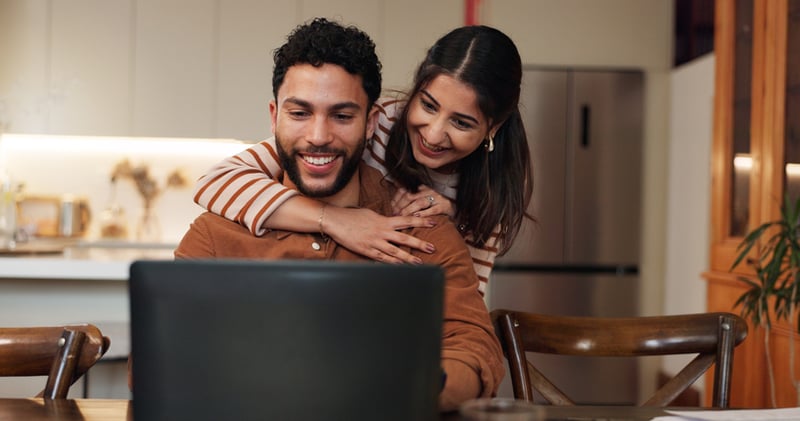 A man and woman smile while looking at a laptop.