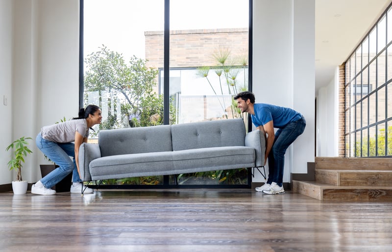 A man and a woman carry a couch into a new home.
