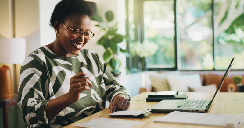 A woman smiles at a laptop while calculating savings from her down payment and mortgage discount points.