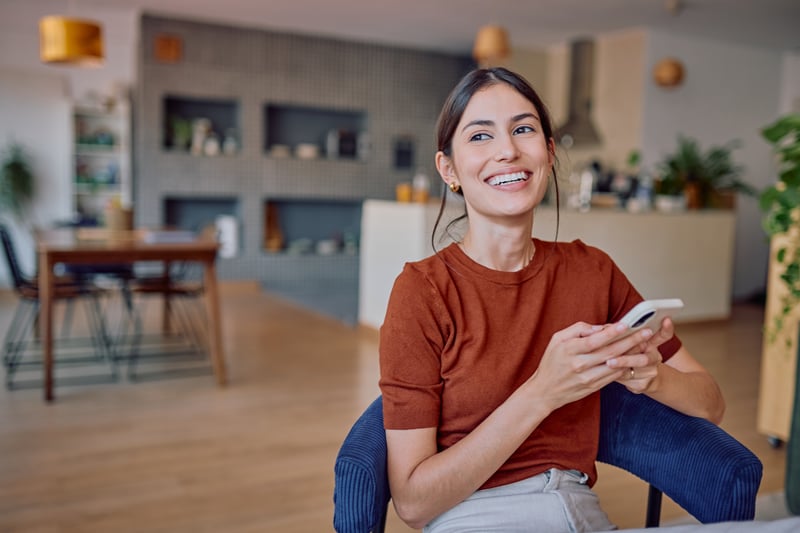 A woman smiles while learning about DSCR loan requirements on her phone.