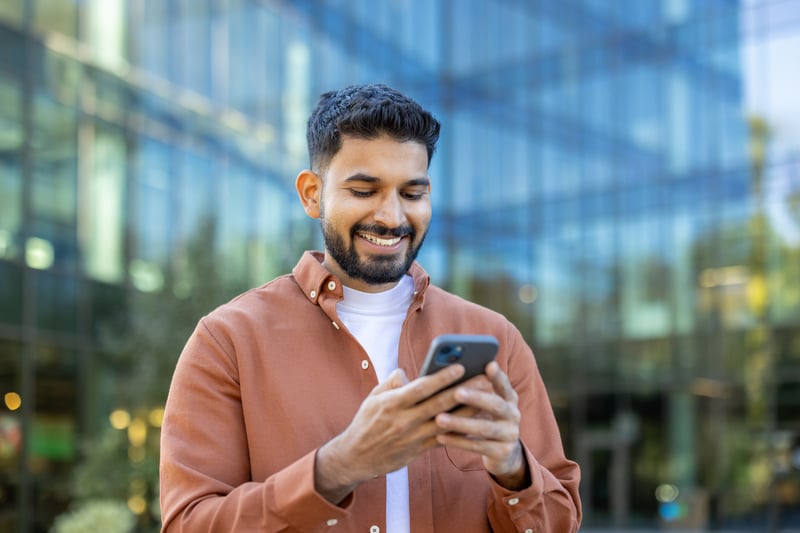 A man smiles at a cell phone while reviewing Ohio refinance rates.