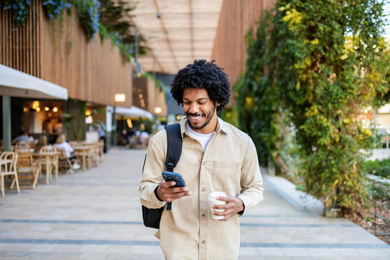 A man smiles at a cell phone in a mall.