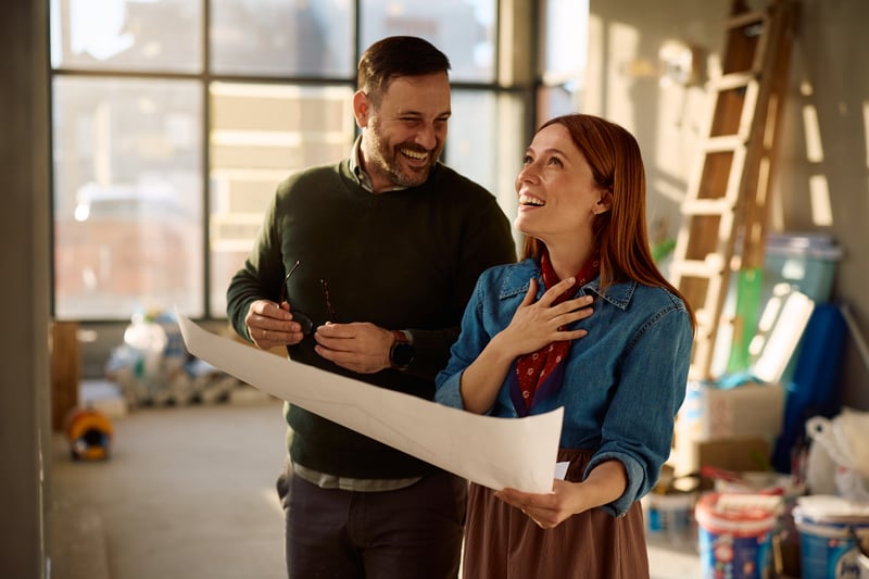 A man and a woman smile while supervising home renovations.