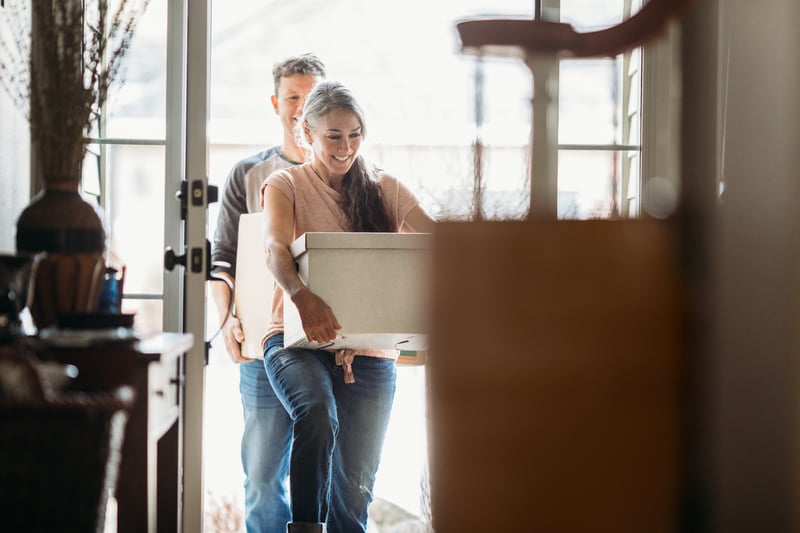 A man and a woman carry boxes into a new house.