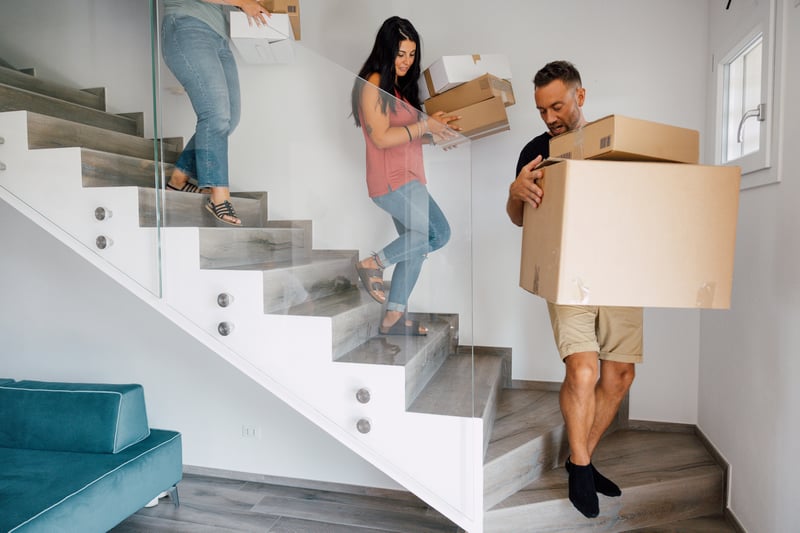 People carry boxes down stairs into a new house.