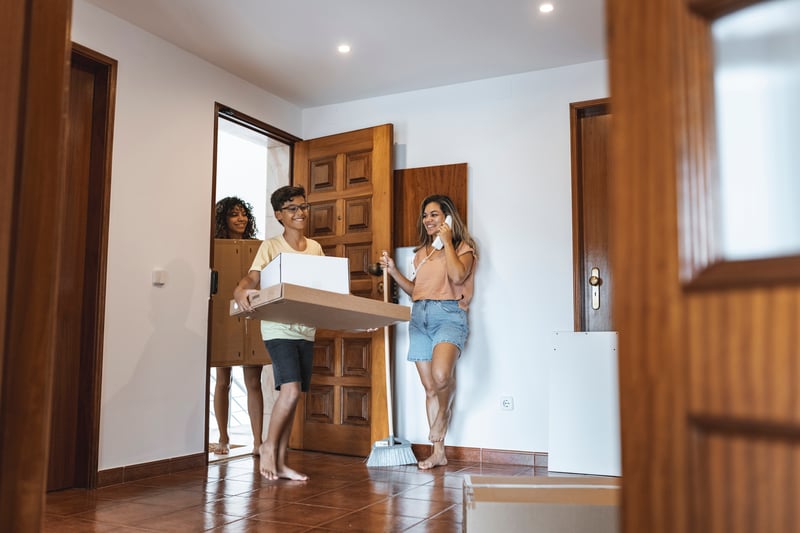 People smile while carrying boxes into a new house.