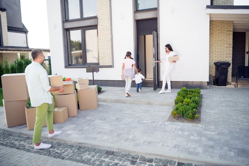 People stand outside of a new house surrounded by moving boxes.