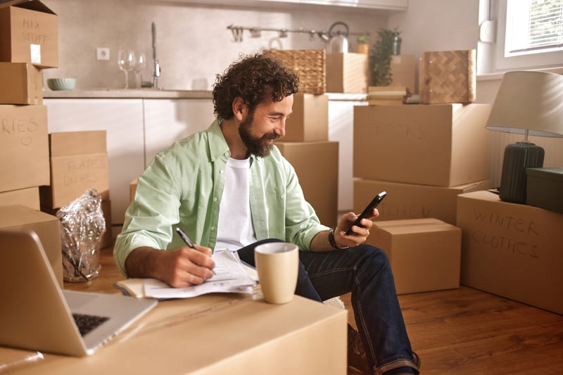 A man drinks coffee and looks at his phone while sitting on a couch surrounded by coffee.