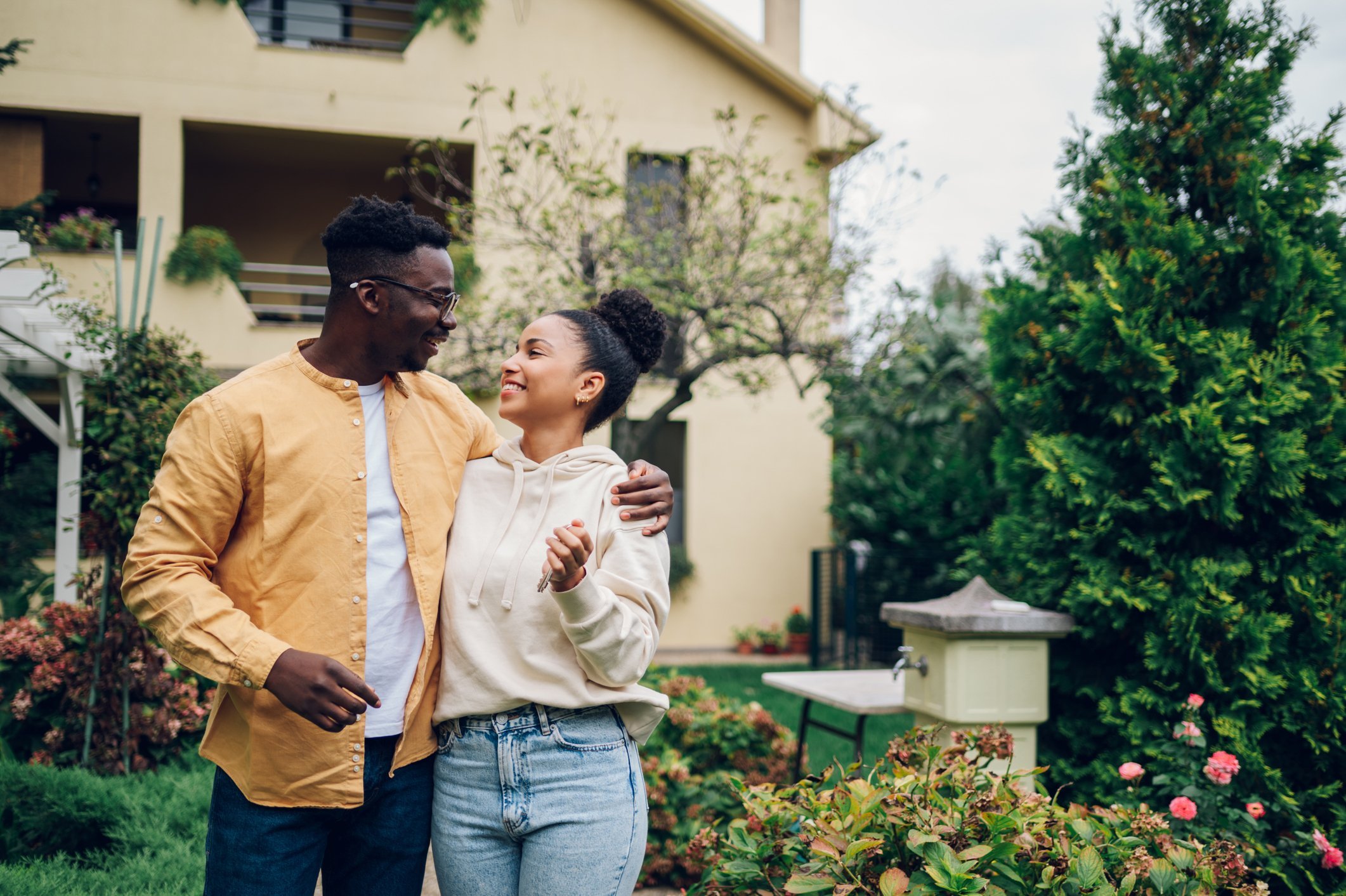 A man and a woman smile outside of a house.