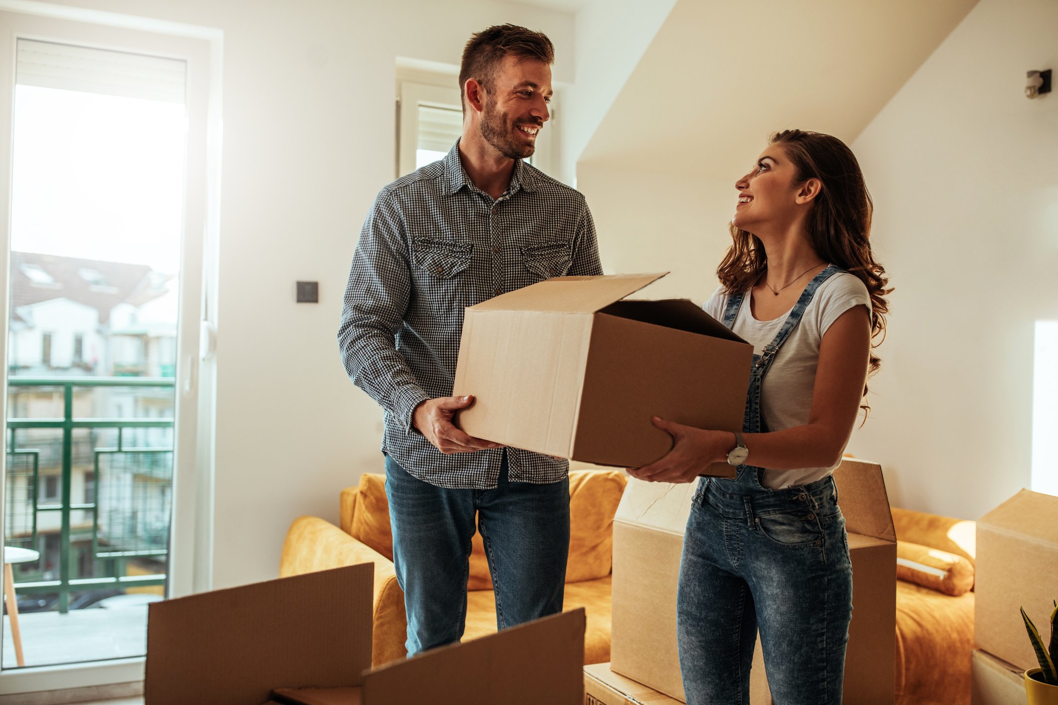 A man and a woman smile while carrying a box into a house.